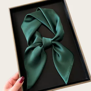 Close-up of an elegant emerald green satin square scarf tied in a bow on a black tray