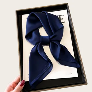 Detailed view of an elegant dark blue silk scarf bow on a white magazine in a box