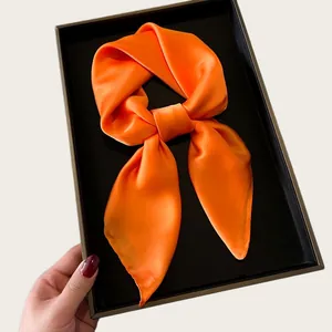 Close-up of vibrant orange silk square scarf tied in a knot on a luxury black tray