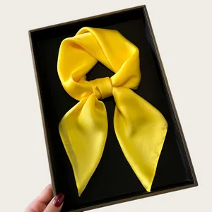 Detailed view of a vibrant yellow satin square scarf tied in a bow on a black tray