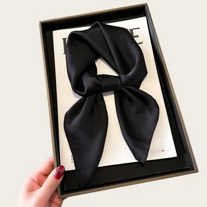 Elegant black silk square scarf tied in a bow displayed on a minimalist white background