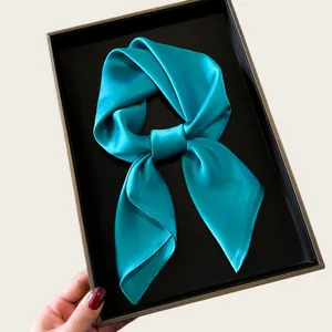 Detailed view of a shiny cyan teal silk square scarf tied in a bow inside a black gift box