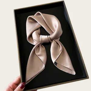 Detail shot of a luxurious cream-colored silk scarf elegantly folded in a black gift box.