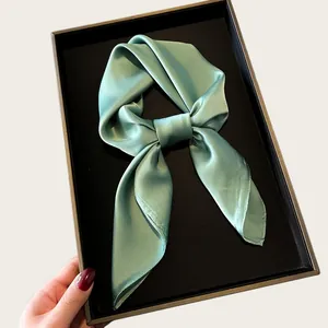 Detail shot of a soft sage green silk scarf elegantly folded in a black gift box