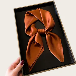 Close-up of a rust orange silk square scarf tied in a bow on a display box
