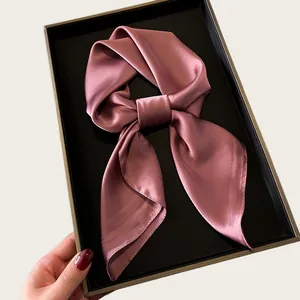 Detailed macro shot of a silky pink square scarf inside a luxury black gift box
