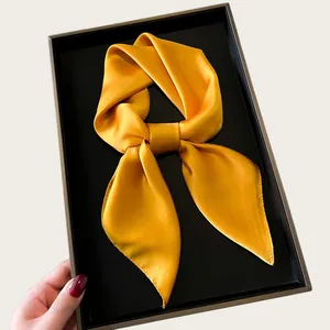 Golden silk square scarf tied in a bow shape presented in a sleek black display box
