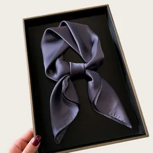 Close-up of a luxurious grey silk neck scarf tied in a knot in a black tray.
