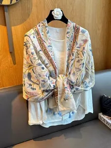 Close-up of lightweight floral shawl with cream base, colorful botanical print and tassels