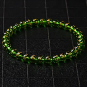 Macro detail of green cat's eye beads bracelet with golden engraved spiritual symbols.