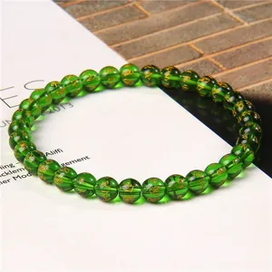 Close-up of 6mm green beaded bracelet with gold mantra engravings on lifestyle magazine.
