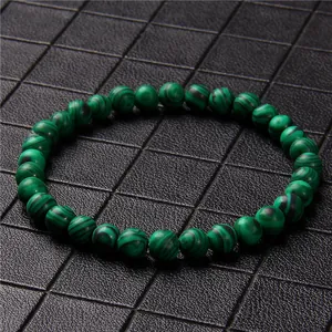 Macro detail of a 6mm green malachite stone beaded bracelet on a black grid mat