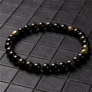 Macro detail of 6mm black obsidian stone beads with golden sheen on a dark grid background.