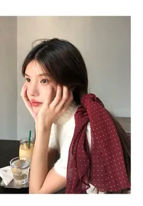 Primo piano di un foulard in seta bordeaux a pois usato come nastro per capelli