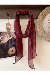 Dettaglio di un foulard di seta bordeaux a pois elegantemente drappeggiato su un gancio in legno