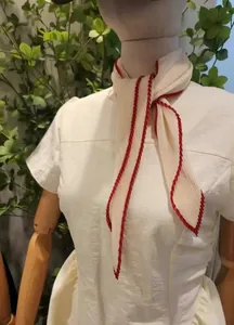 Detailopname van een crème geplooide skinny sjaal met decoratieve rode geschulpte randen