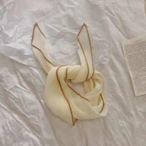 Close-up detail van de crèmekleurige geplooide zijden sjaal met bruine contrastrand
