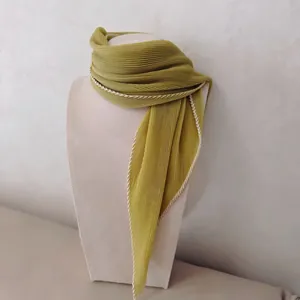 Detailopname van een geplooide mosterdgele zijden sjaal op een buste met fijne textuur.