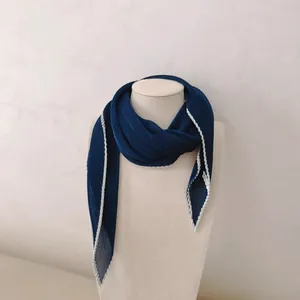 Detailopname van een donkerblauwe geplooide zijden sjaal met witte randen op een buste.