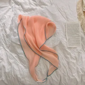 Detail van roze geplooide zijden sjaal met blauwe bies op witte zachte stof