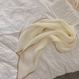 Gedetailleerd beeld van crème geplooide sjaal met een elegante gouden koordrand afwerking