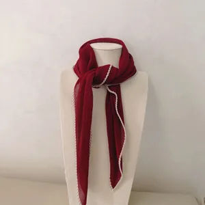 Detail van een elegante geplisseerde bordeauxrode sjaal met een crèmekleurige schulprand