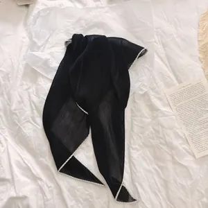 Detailopname van een elegante zwarte geplooide sjaal met witte gevlochten rand