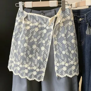 Dettaglio di un coprigonna in pizzo floreale bianco indossato su pantaloni grigi.