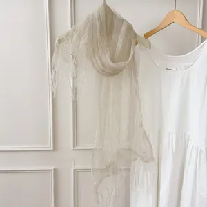 Detailed view of a lightweight sheer ivory faux silk scarf featuring delicate tassels