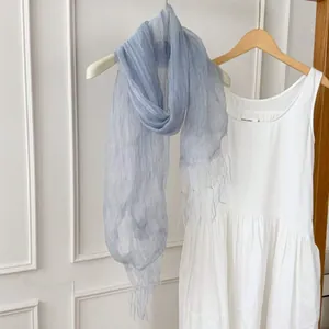 Detailed view of a light blue sheer scarf with tassels paired with a white dress background