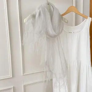 Detail of a lightweight sheer silk-like scarf with tassels hanging against a white wall