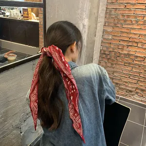 Dettaglio di un foulard di seta rosso vintage con motivo paisley usato come fascia per capelli.