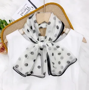 Close-up of a elegant black polka dot chiffon scarf tied in a bow on a white top