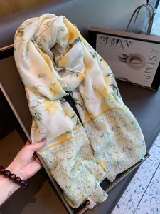 Detailed view of a lightweight floral scarf with yellow flowers and white tassels at the corners.