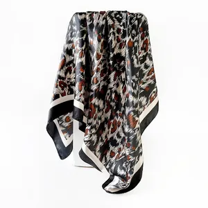 Close-up of glossy leopard print satin square scarf with elegant draped fabric texture.
