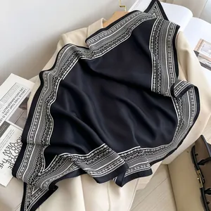 Close-up of a black silk scarf with white paisley pattern draped over a beige blazer.