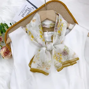 Close-up of a floral print silk scarf twilly tied in a bow on a white dress neckline view