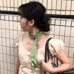 Close-up of a green ramie skinny scarf worn with a beige puffed-sleeve top.