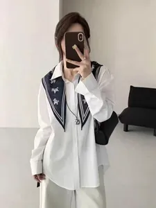 Détail d'un foulard en soie bleu marine à imprimé poney porté sur une chemise blanche.