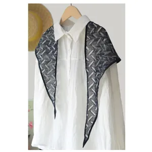 Dettaglio di una sciarpa triangolare in pizzo nero con paillettes su una camicia bianca.