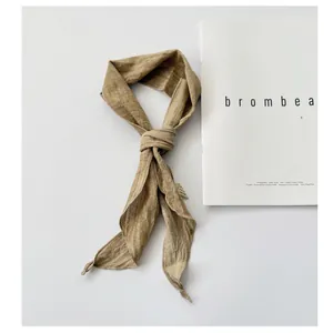 Detail shot of a textured khaki ramie thin scarf tied in a knot on white background