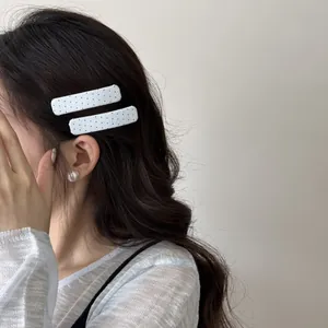 Detailopname van twee witte haarspeldjes met stippen op golvend bruin haar.