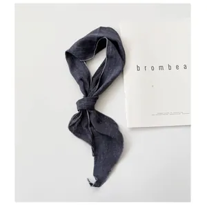 Detail of a dark grey ramie skinny scarf with a knotted design on a white background.