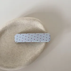 Detailopname van een blauwe stoffen haarclip met rode stippen op een beige plateau