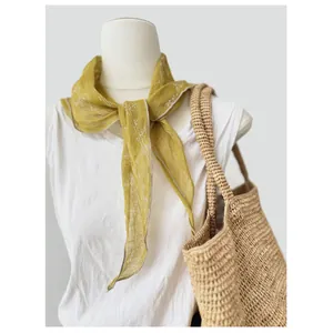 Primo piano di un foulard a triangolo in puro lino giallo senape con motivi su un manichino bianco.