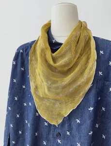 Dettaglio di un foulard a triangolo in lino giallo senape con ricami bianchi su denim.