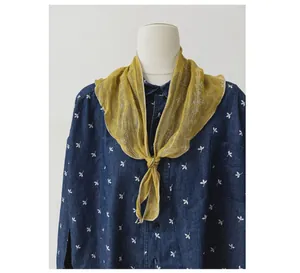 Dettaglio di un foulard in lino giallo annodato al colletto di una camicia blu