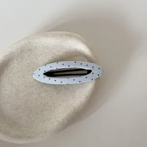 Detail van een lichtblauwe stoffen BB-haarclip met stippen op een beige keramische schaal.