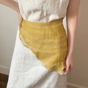 Detailed macro view of a vintage yellow linen floral wrap styled over a beige dress.