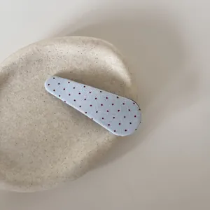 Detailopname van een lichtblauwe stoffen haarclip met rode stippen op stenen ondergrond